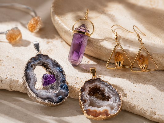 Handcrafted Brazilian natural stone jewelry with amethyst, geode, citrine, gold and silver plated details on a beige stone surface.