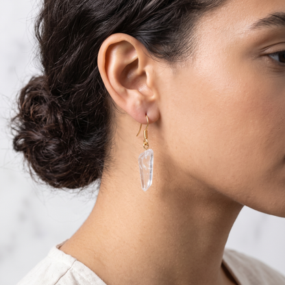 ide profile close-up of a model wearing a gold-plated natural clear quartz crystal point drop earring, showcasing its elongated shape and clarity.